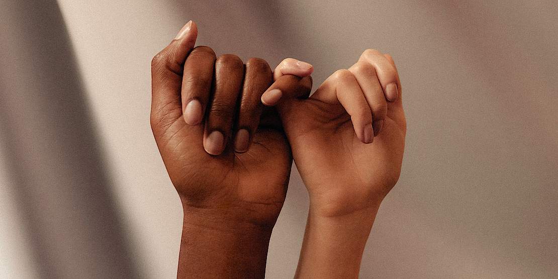 Eine Hand einer Person of Color und die einer weißen Person, am kleinen Finger eingehakt